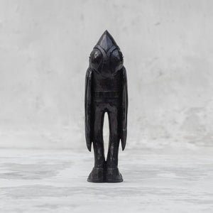 Back view of a black wooden raven person statuette  against a light gray background