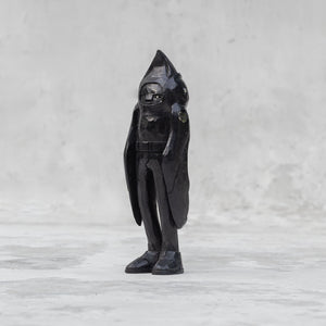 A black wooden raven person statuette  facing sideways against a light gray background