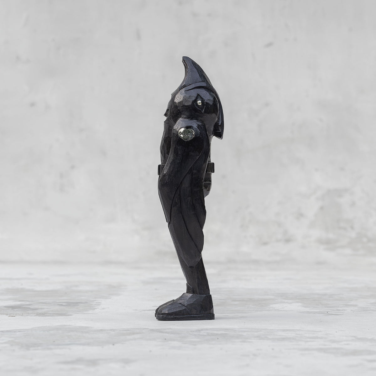 Side view of a black wooden raven person statuette  against a light gray background