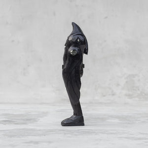 Side view of a black wooden raven person statuette  against a light gray background