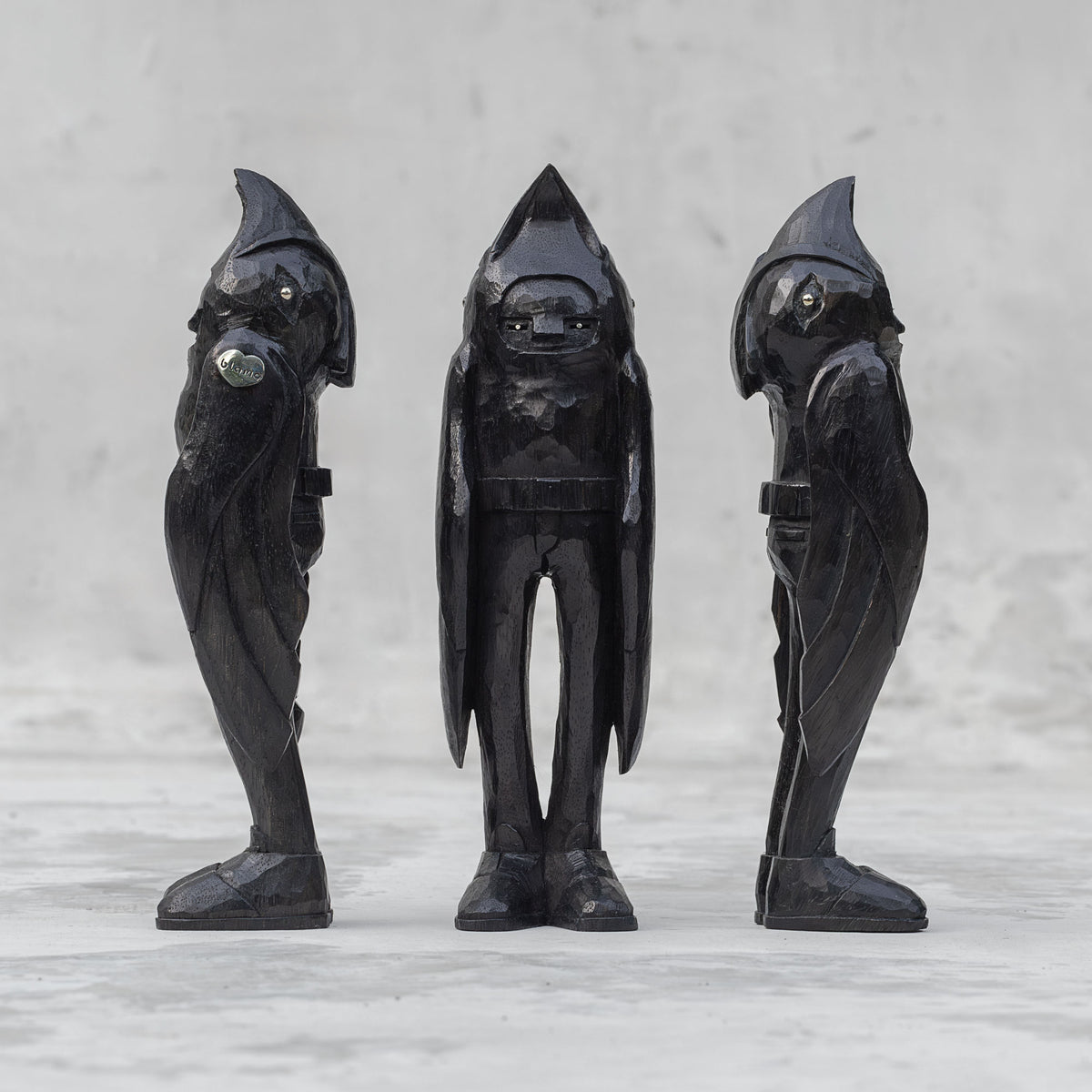 3 black wooden raven person statuettes facing different directions against a light gray background