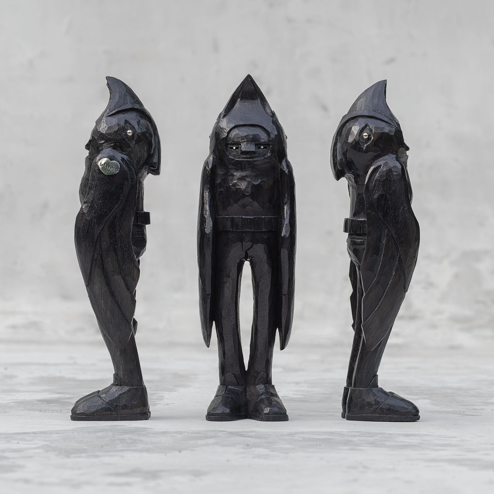 3 black wooden raven person statuettes facing different directions against a light gray background