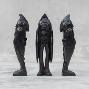 3 black wooden raven person statuettes facing different directions against a light gray background