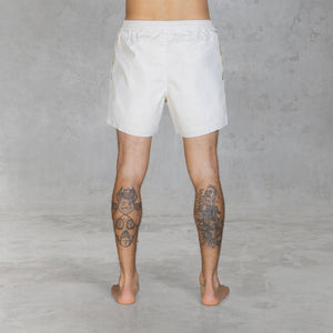 Back view of a person from feet to waist wearing mid-thigh shorts in hand painted bone against a gray background