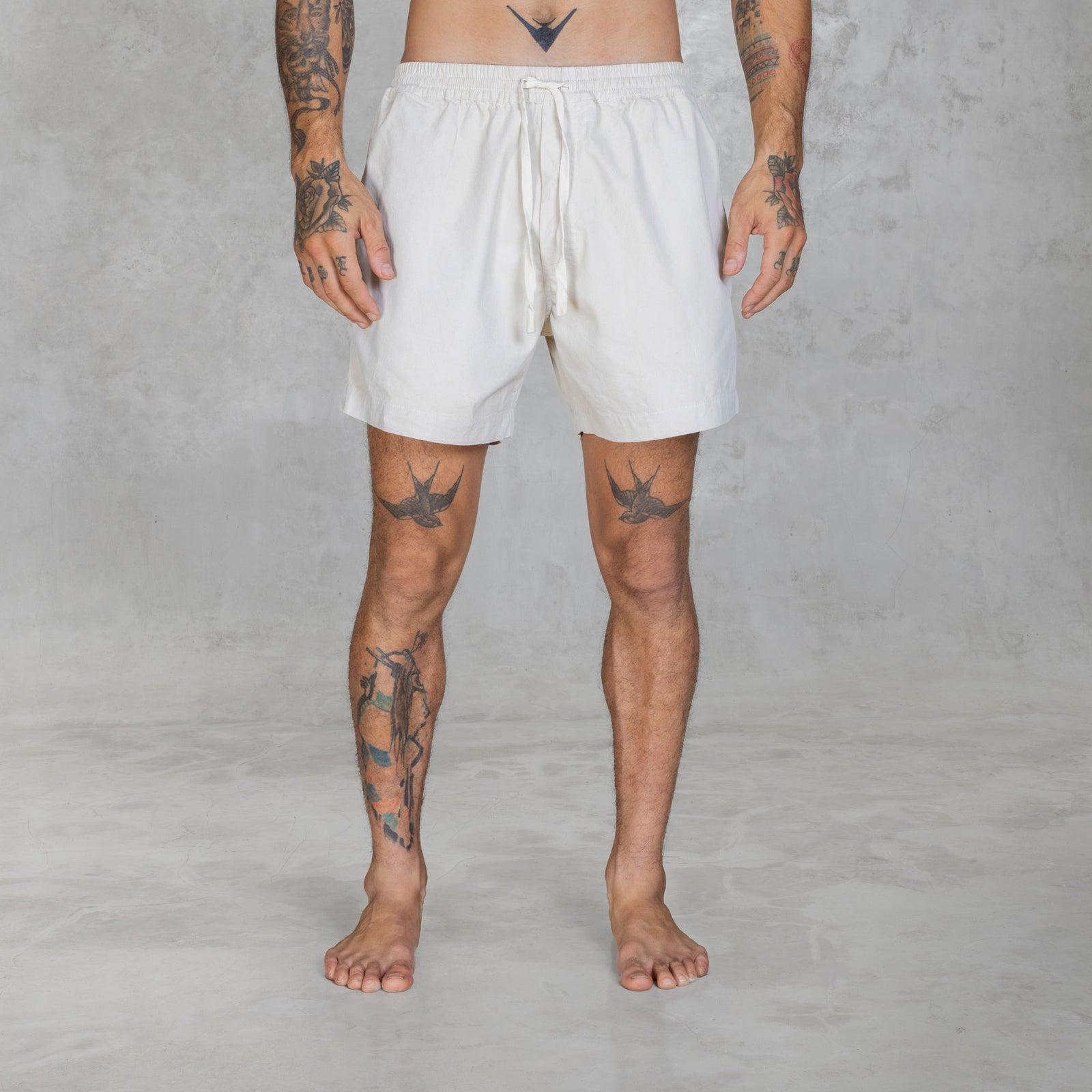 Person from feet to waist wearing mid-thigh shorts in hand painted bone against a gray background