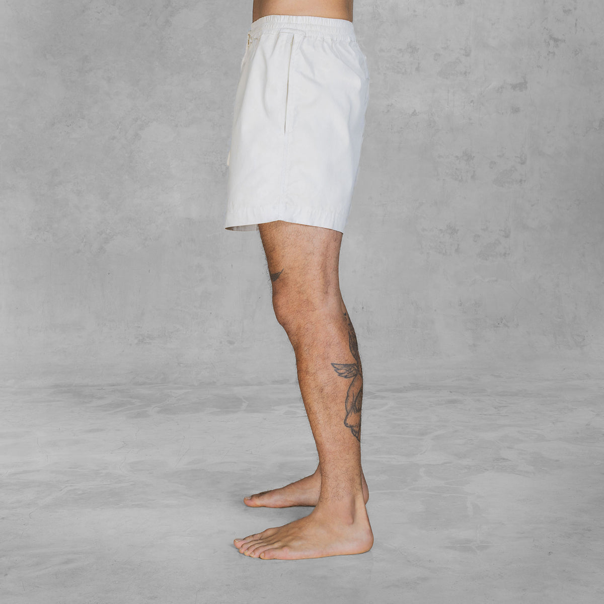 Side view of a person from feet to waist wearing mid-thigh shorts in hand painted bone against a gray background