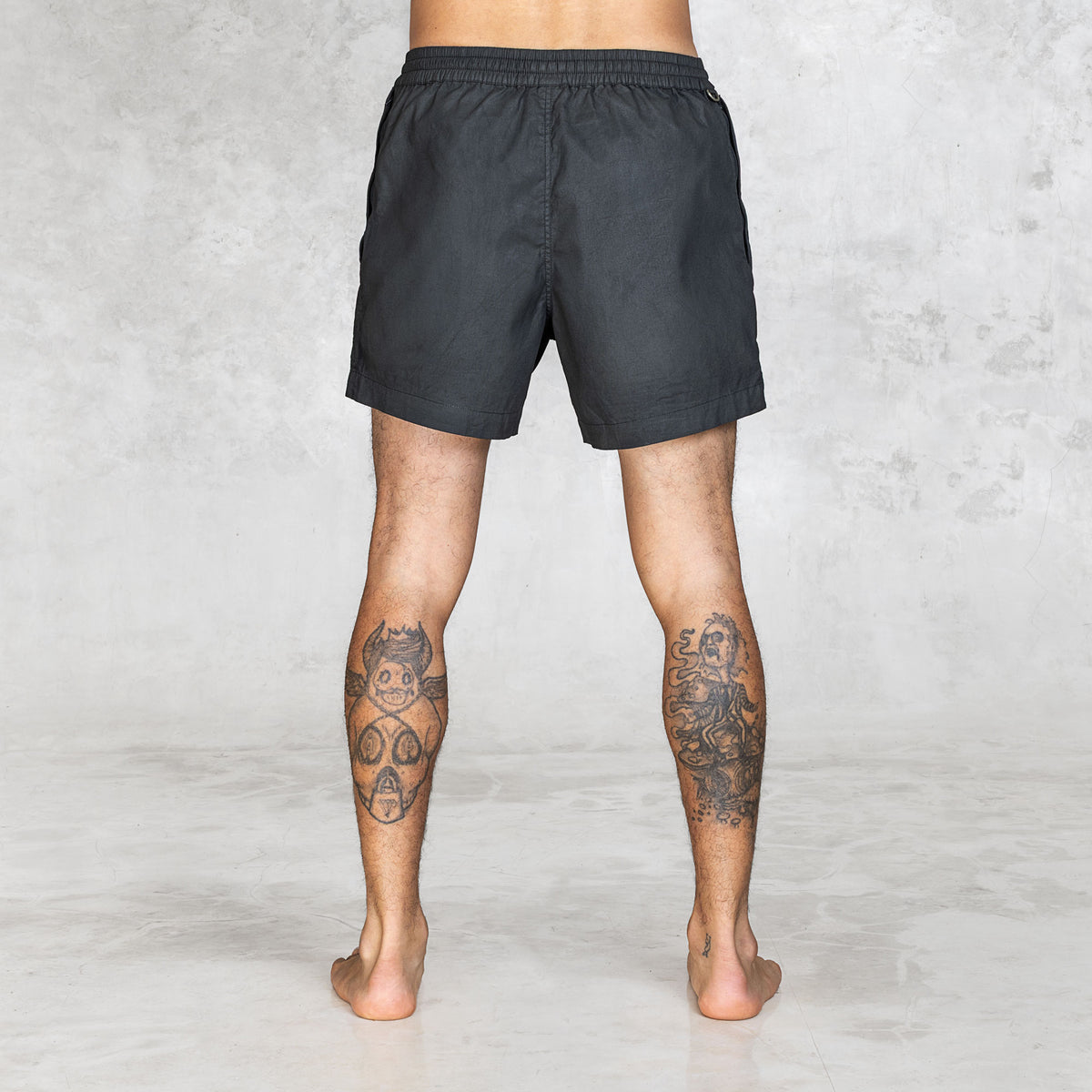 Back view of black stretch canvas shorts highlighting no-back-pocket construction and elastic waistband.