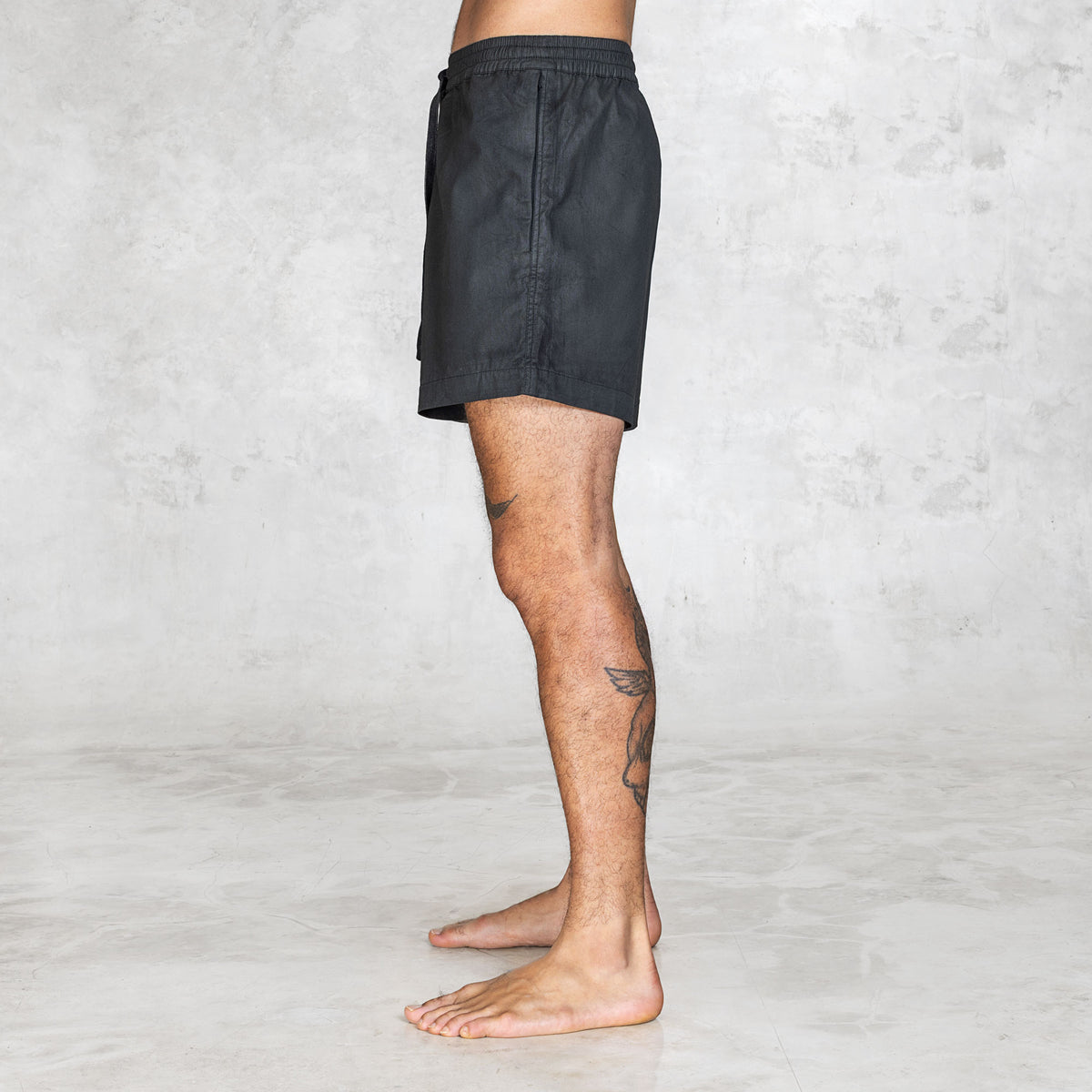 Side view of black mid-thigh shorts with lightweight zippered pocket and clean no-back-pocket design.