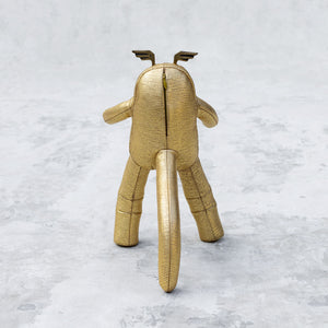 Gold leather and brass plush toy facing backwards on a textured white background