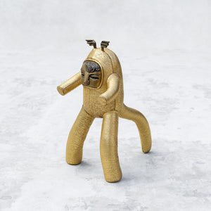 Gold leather and brass plush toy with a tail on a textured white background