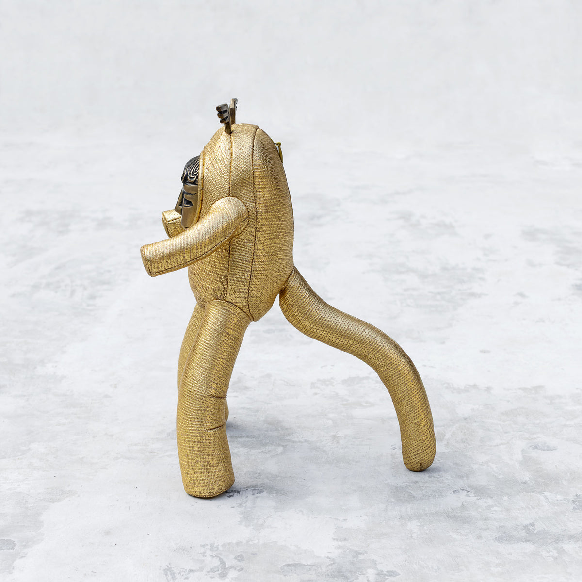 Gold leather and brass plush toy facing sideways on a textured white background