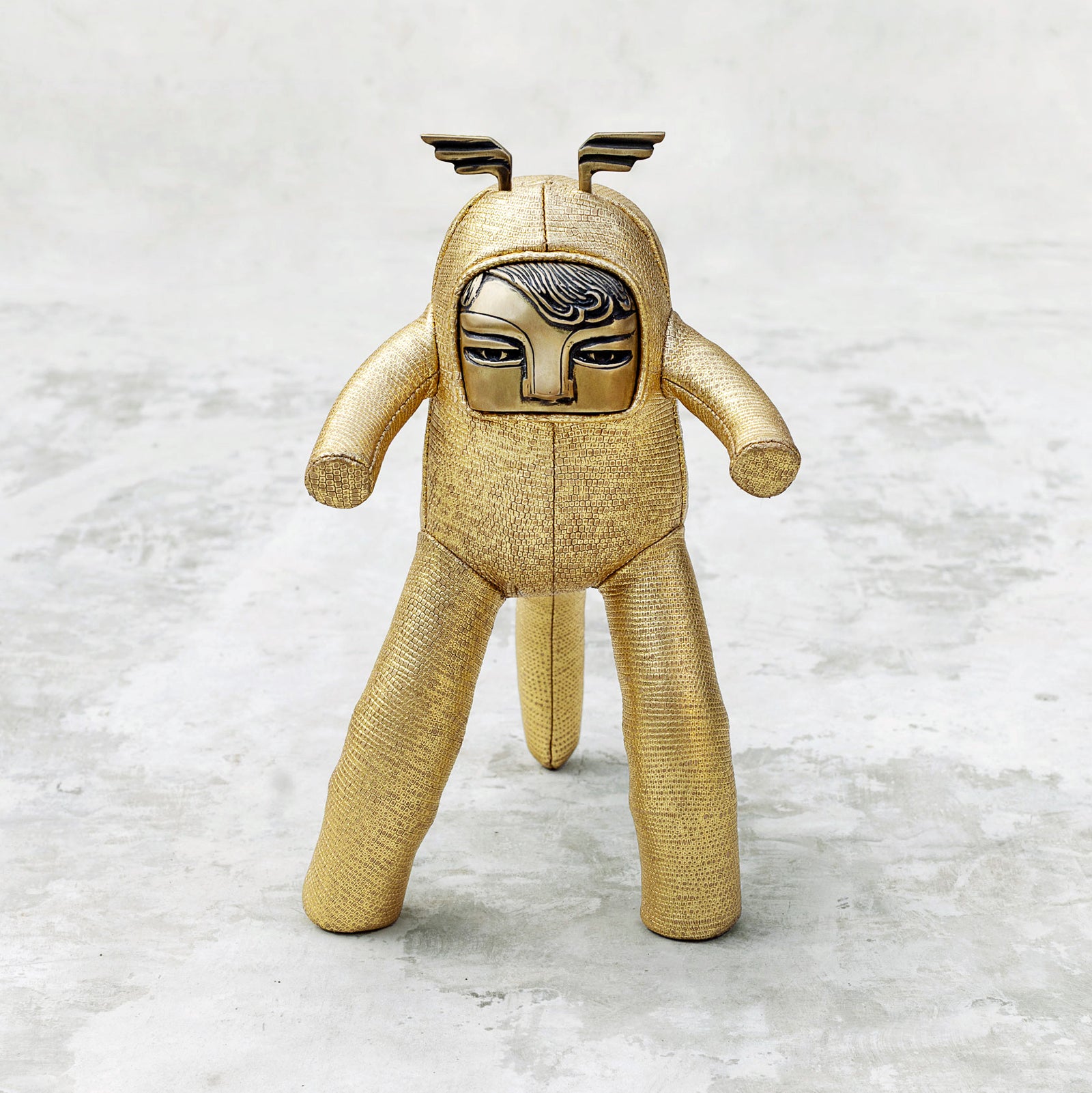 Gold leather body and and brass face plush monkey toy on a textured white background
