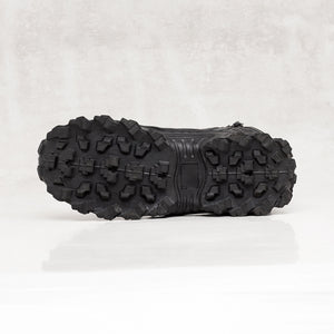 Bottom sole view of a black textured leather boot against a light gray background. 