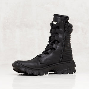 Quarter profile of a black textured leather boot against a light gray background. 