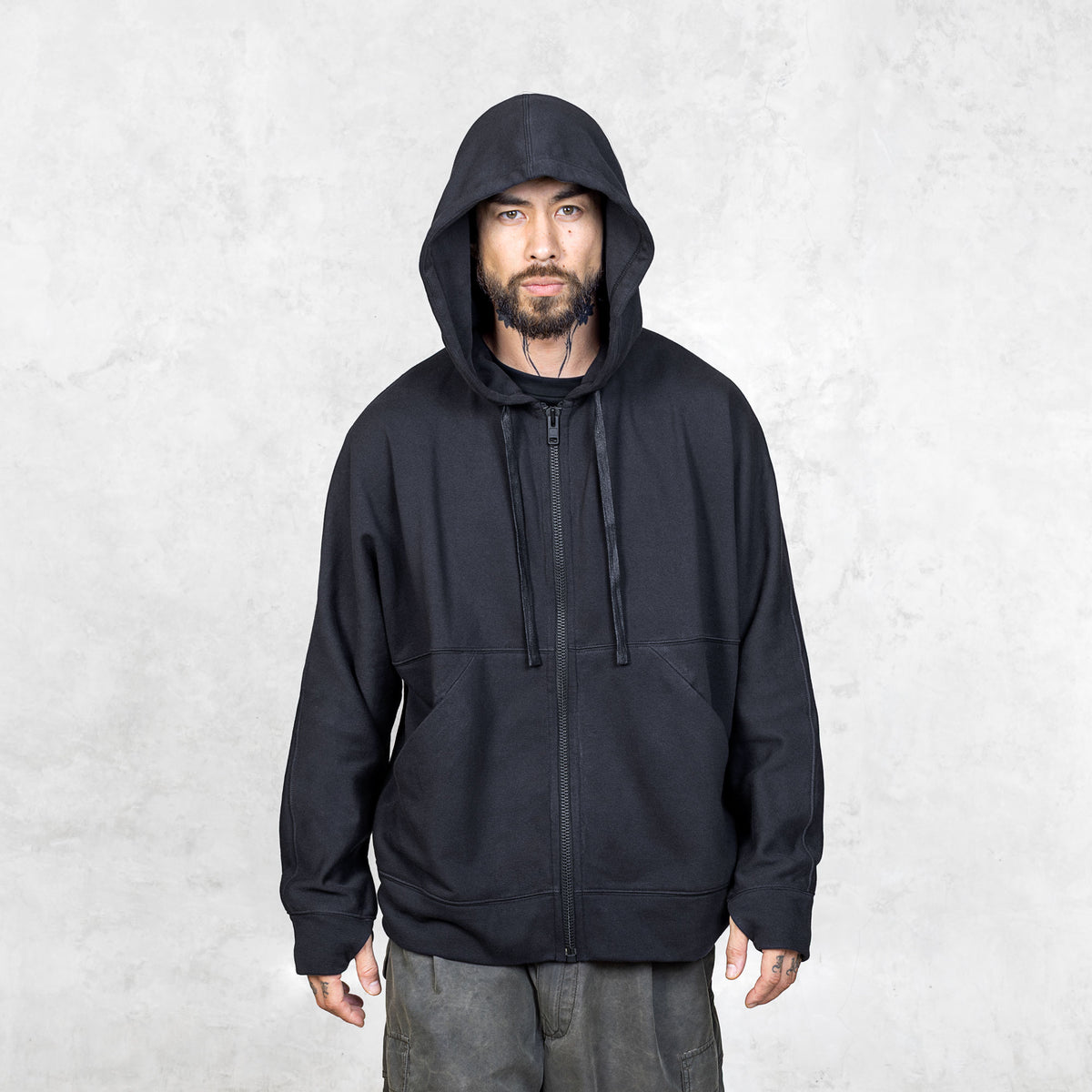 Man wearing a black hoodie with the hood on against a light gray background