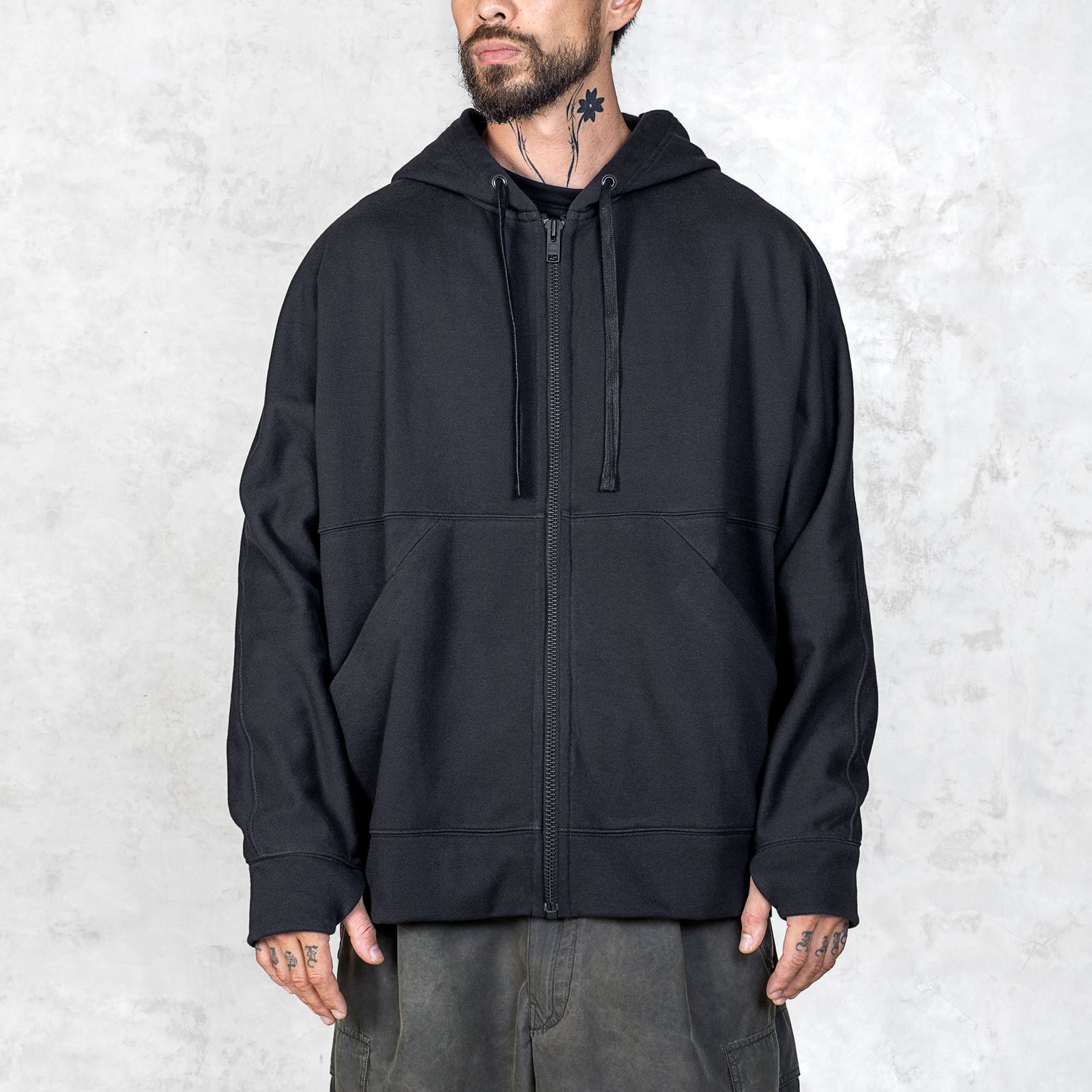 Person wearing a black zip-up hoodie against a light gray background