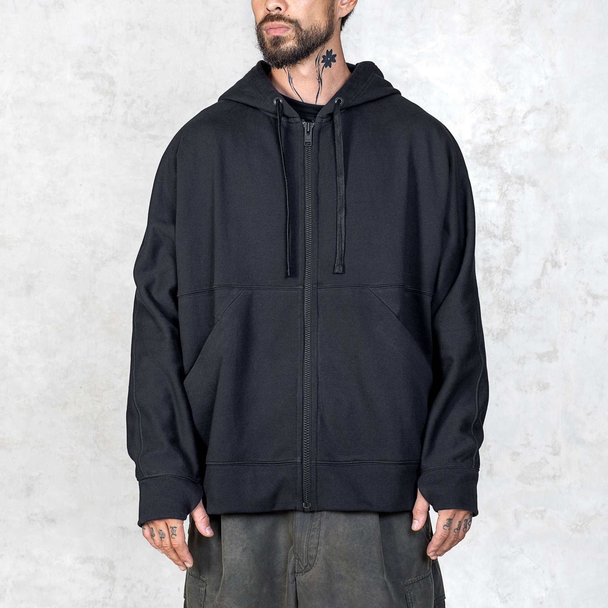 Person wearing a black zip-up hoodie against a light gray background