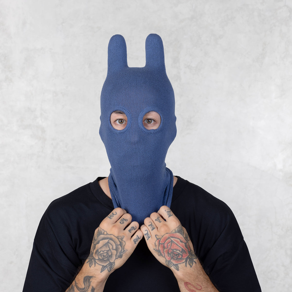 Person wearing a blue knitted bunny mask against a light gray background