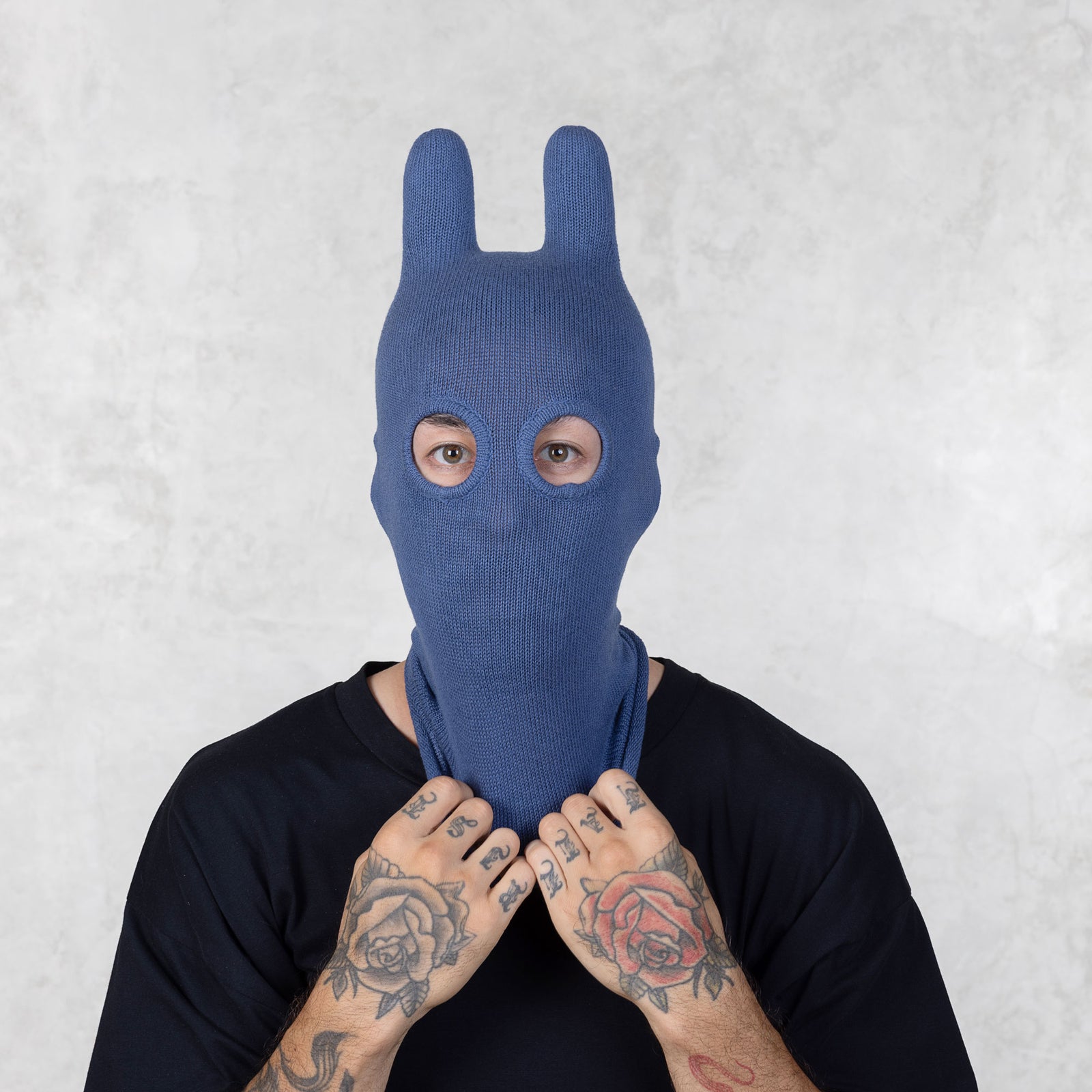 Person wearing a blue knitted bunny mask against a light gray background