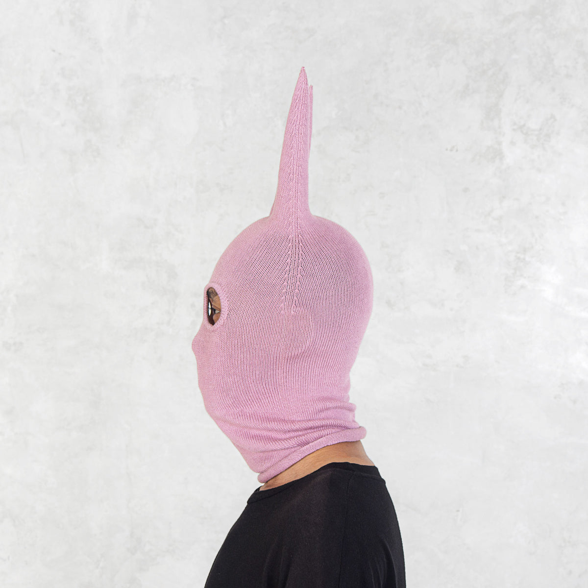 Person facing sideways wearing a pink mask with long spikey ears on a white background
