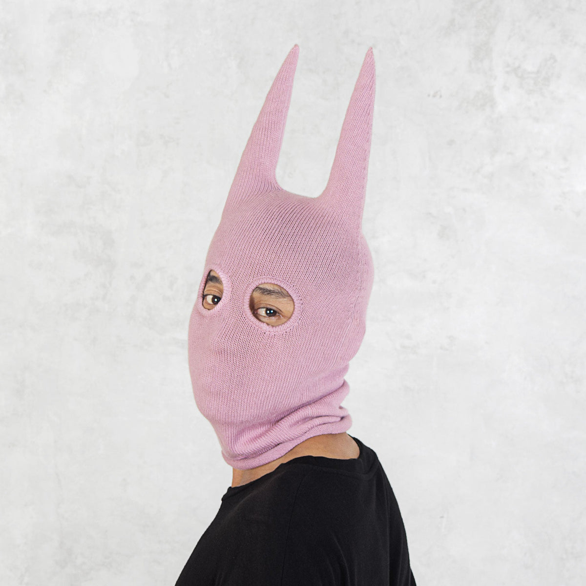 Person wearing a pink mask with long spikey ears on a white background