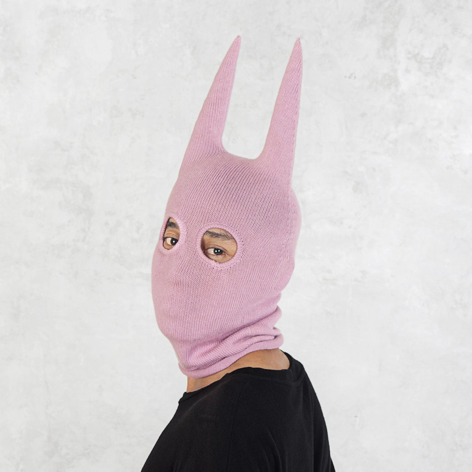 Person wearing a pink mask with long spikey ears on a white background