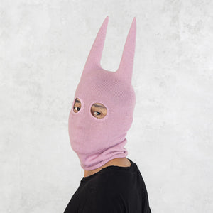 Person wearing a pink mask with long spikey ears on a white background