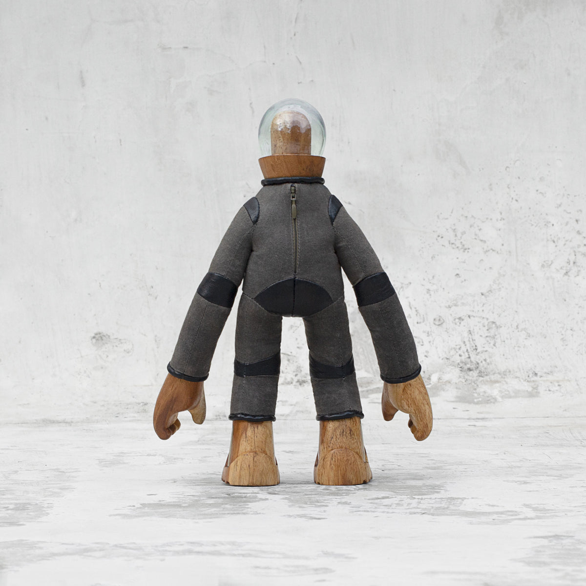 Back view of a leather wood and glass astronaut statuette with a zipper standing against a light gray background
