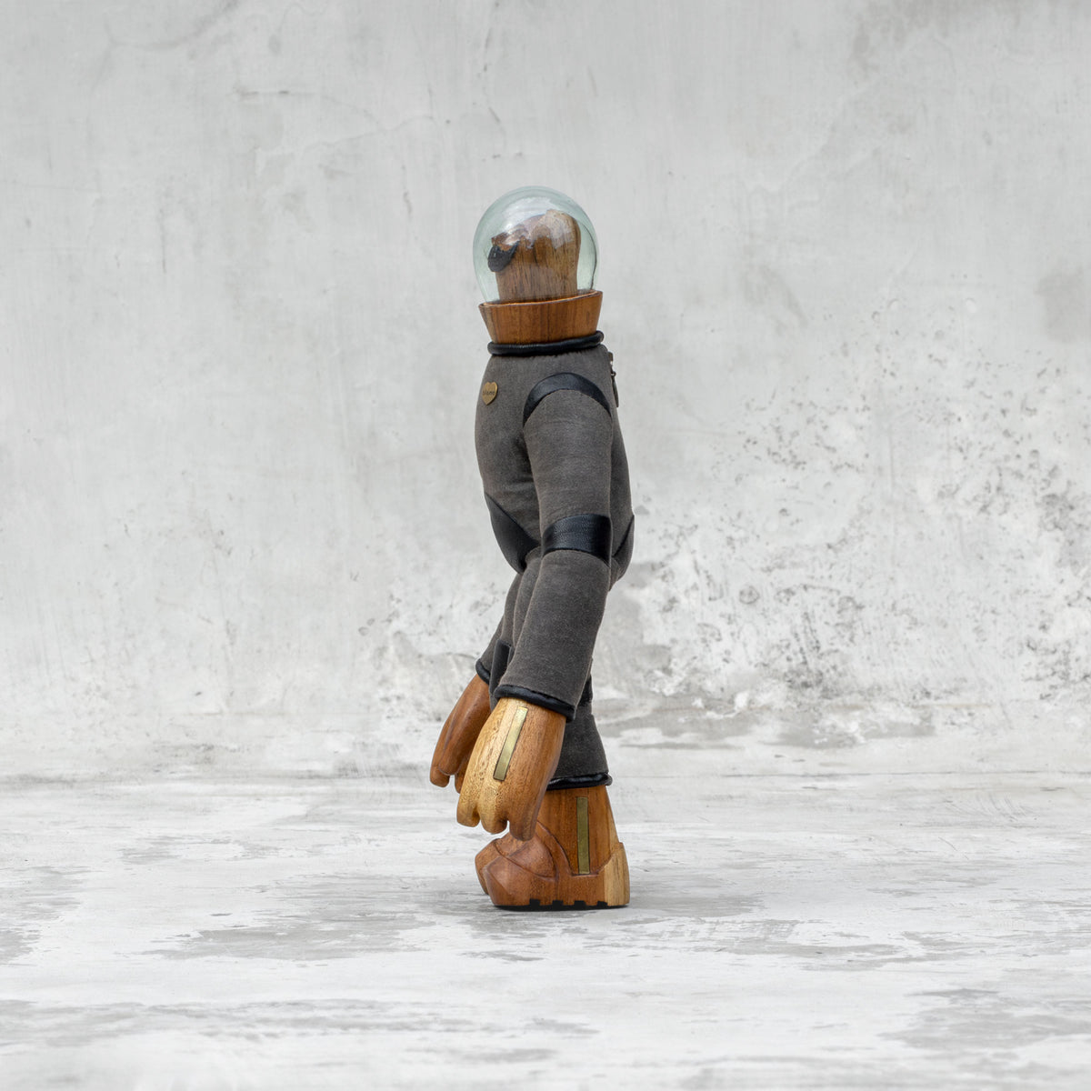 Side view of a leather wood and glass astronaut with a mustache statuette standing against a light gray background