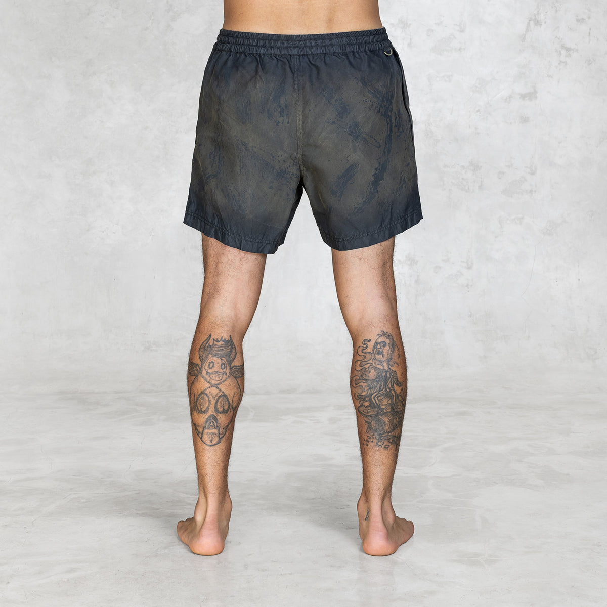 Back view of a Person wearing olive painted swim-like shorts on a plain background