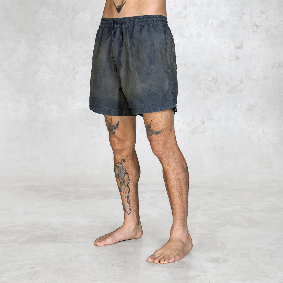 Person wearing dark handpainted swim style shorts on a plain background