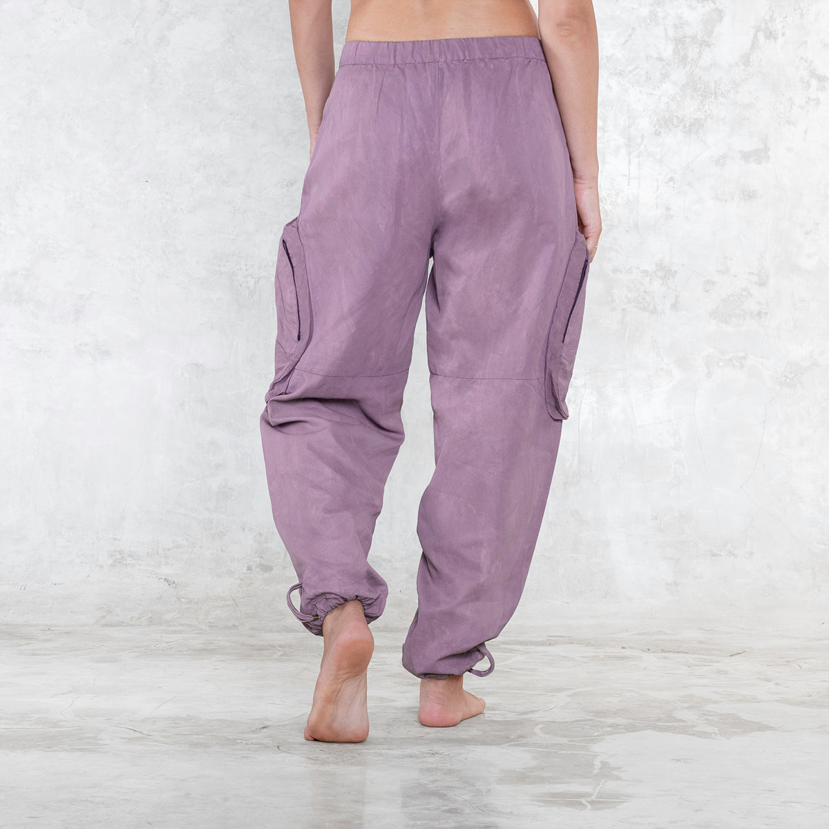 A woman standing facing backwards wearing a pair of dark pink rose silk cargo style BLAMO pants
