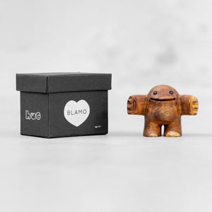 Small wooden sculpture with arms extended in a HUG position and smoky quartz gem eyes and it's box by BLAMO
