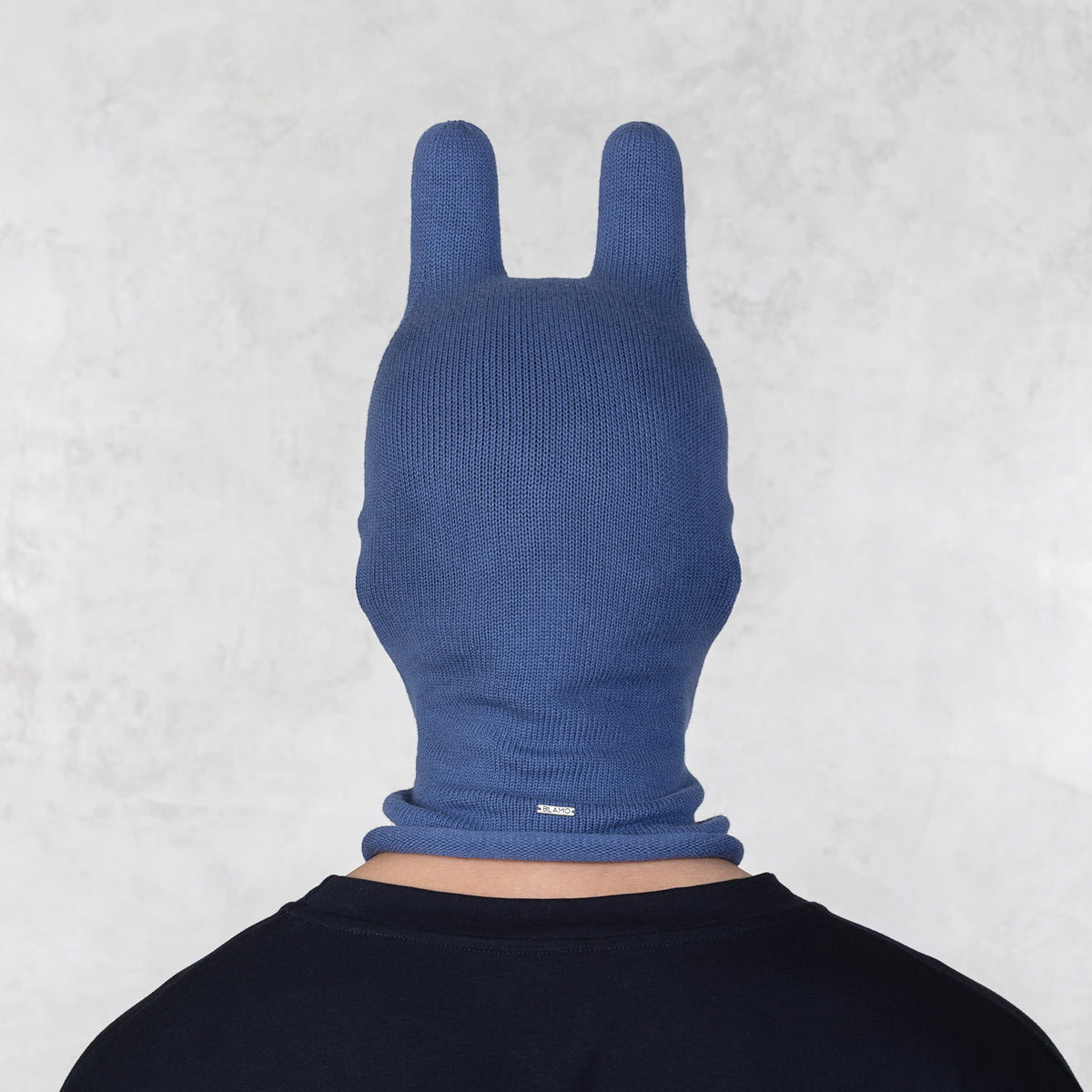 Person wearing a blue knitted mask with ears on a light gray background