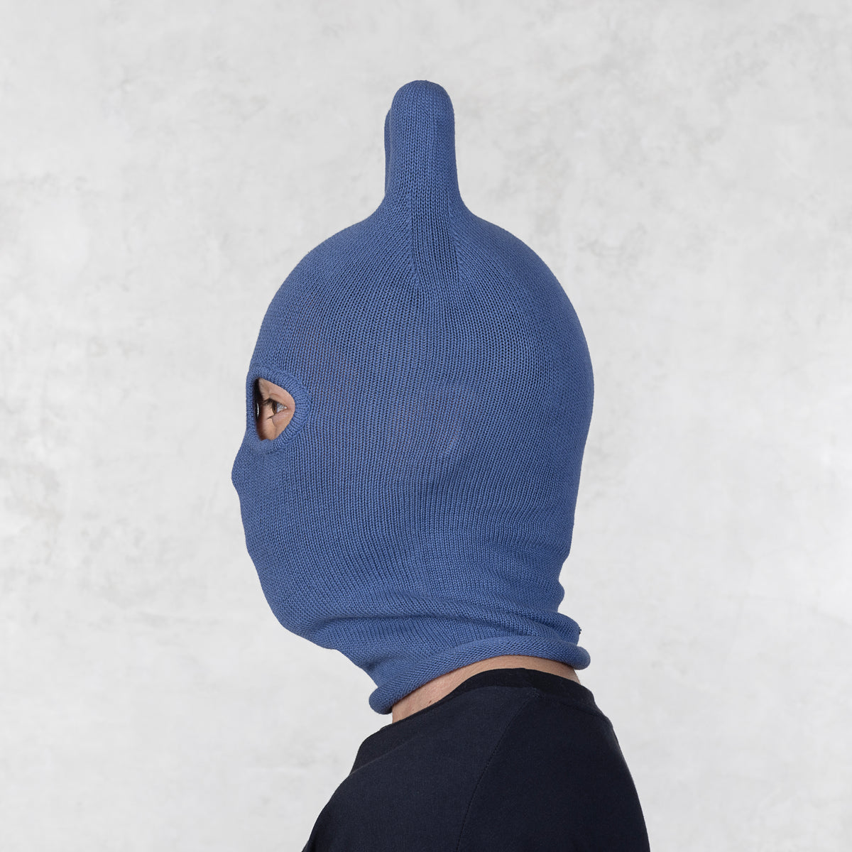 Person wearing a blue knitted balaclava with rounded ears on a light gray background