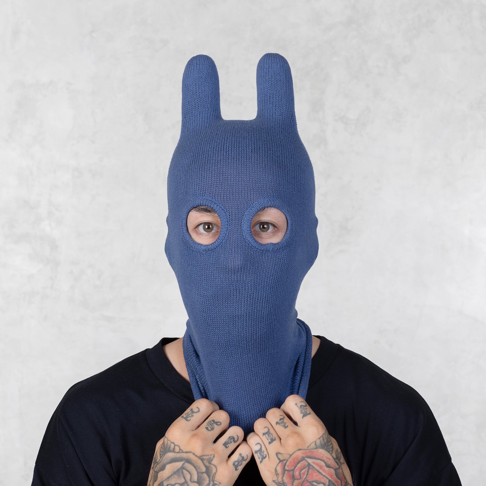 Person wearing a blue bunny mask pulling on the bottom of the mask against a light gray background