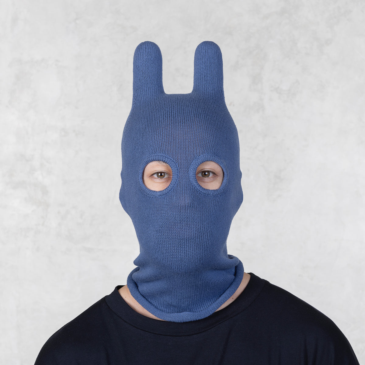 Person wearing a blue knitted bunny mask against a light gray background
