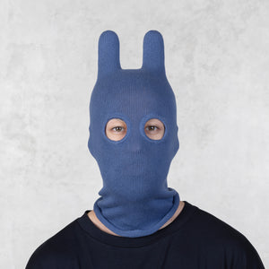 Person wearing a blue knitted bunny mask against a light gray background