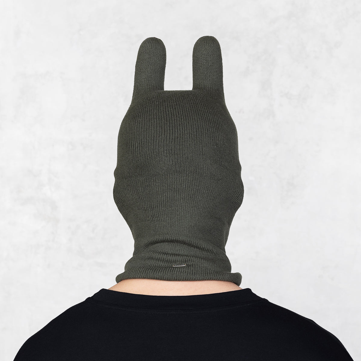 Person wearing a dark green knitted balaclava with ears on a light gray background