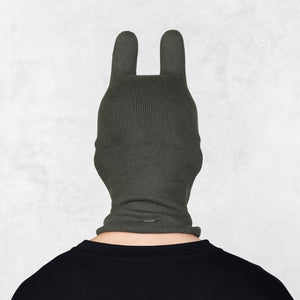 Person wearing a dark green knitted balaclava with ears on a light gray background