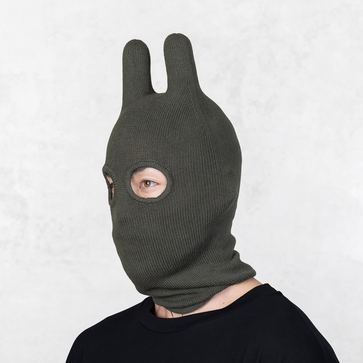 Person wearing a Blamo Socky Dark Olive green knitted balaclava with rabbit ears on a white background
