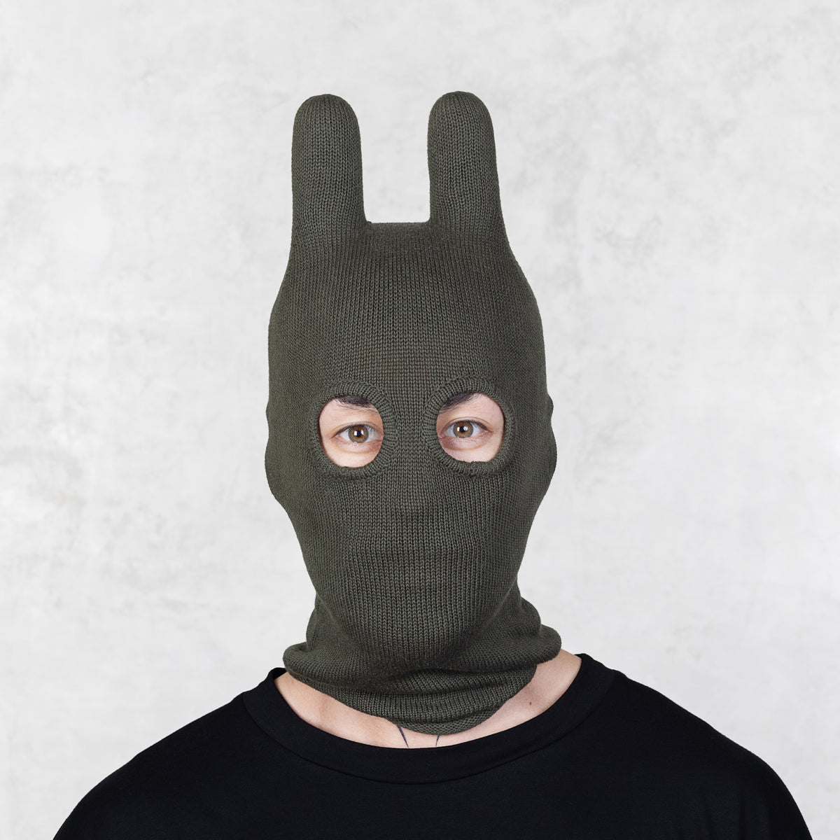 Person wearing a green bunny mask against a light gray background
