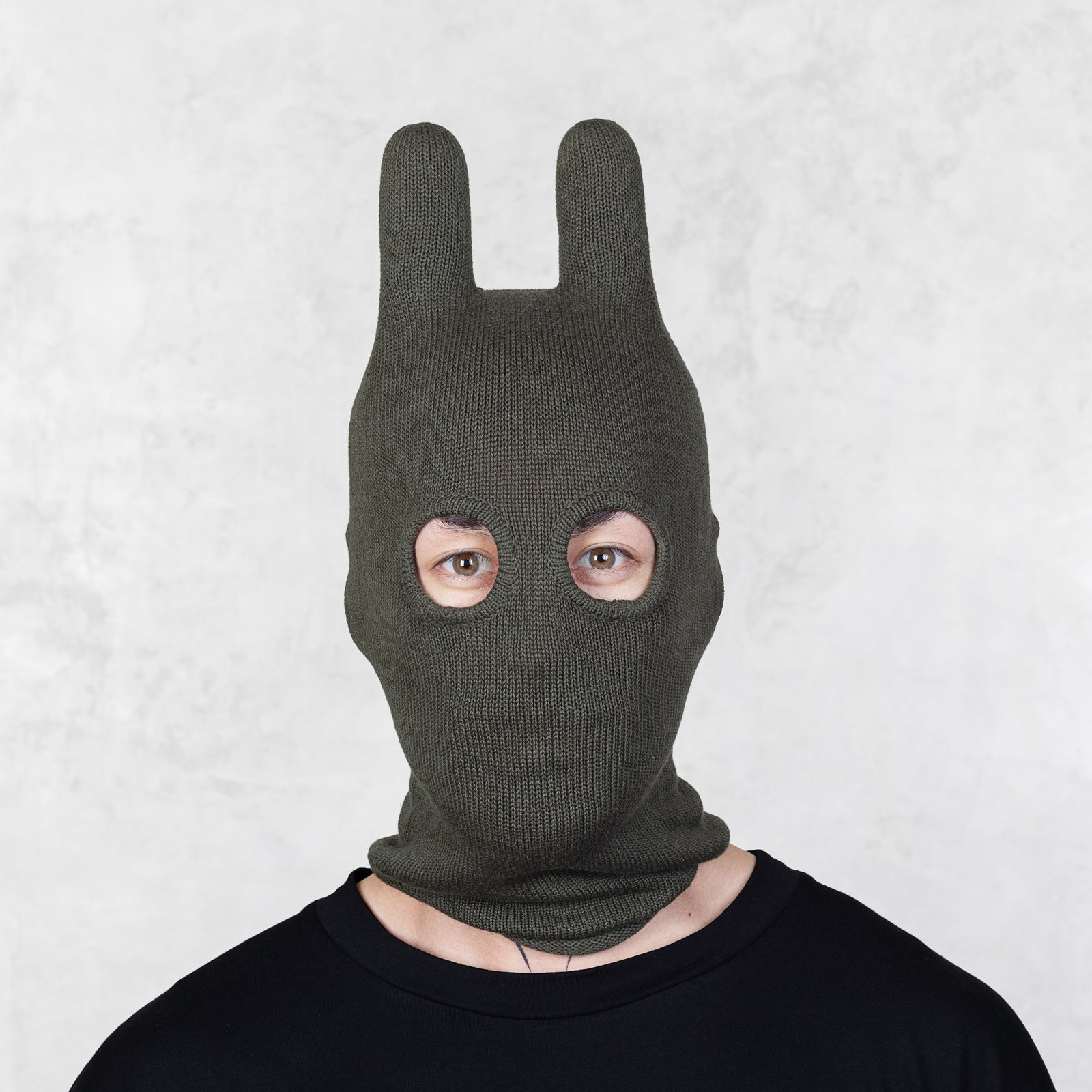 Person wearing a green bunny mask against a light gray background