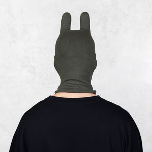 Person wearing a dark green balaclava facing backwards on a light gray background