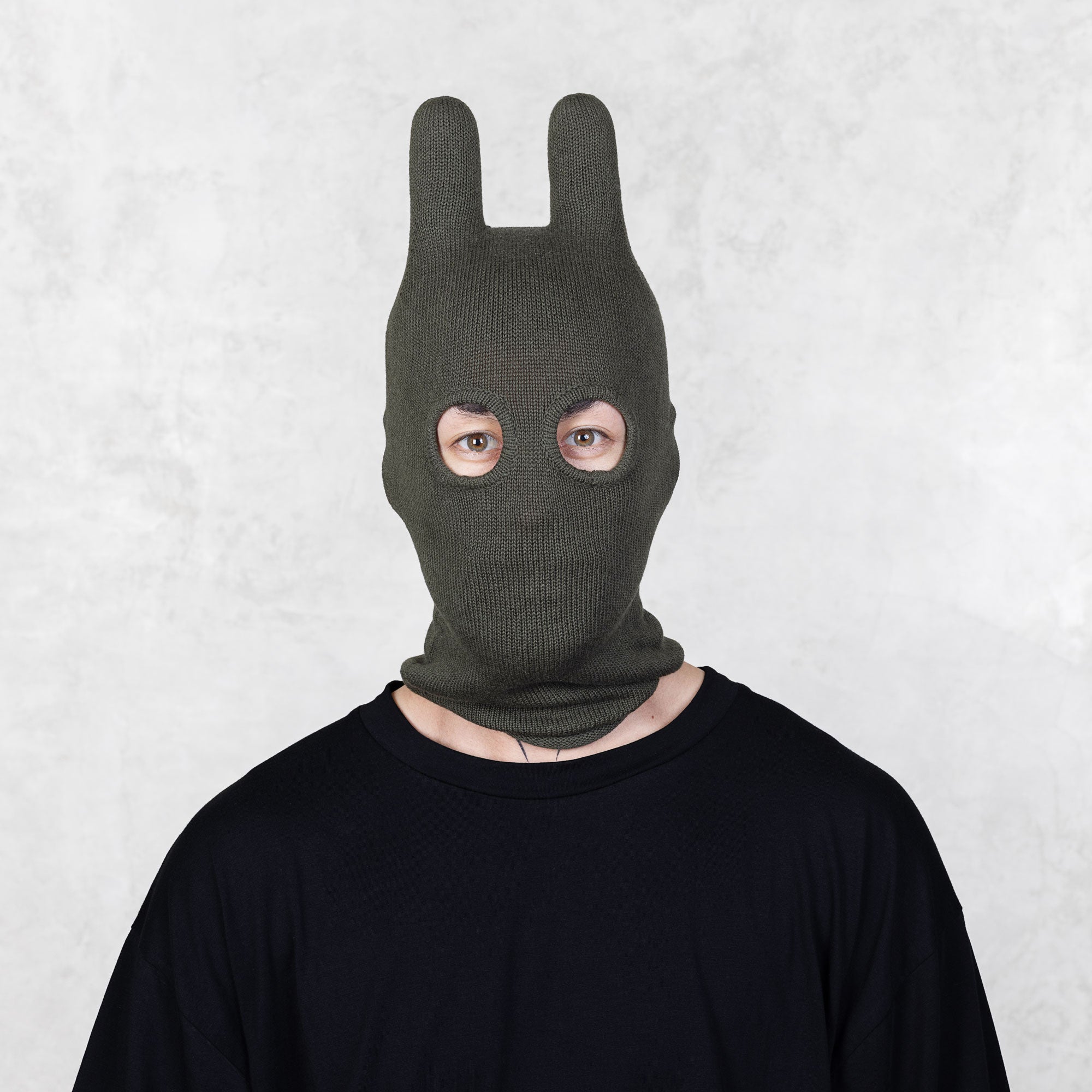 Person wearing a dark green balaclava on a light gray background