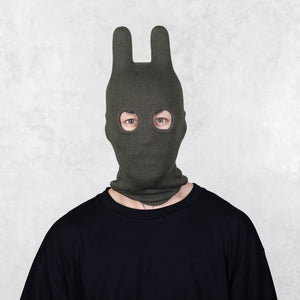Person wearing a dark green balaclava on a light gray background