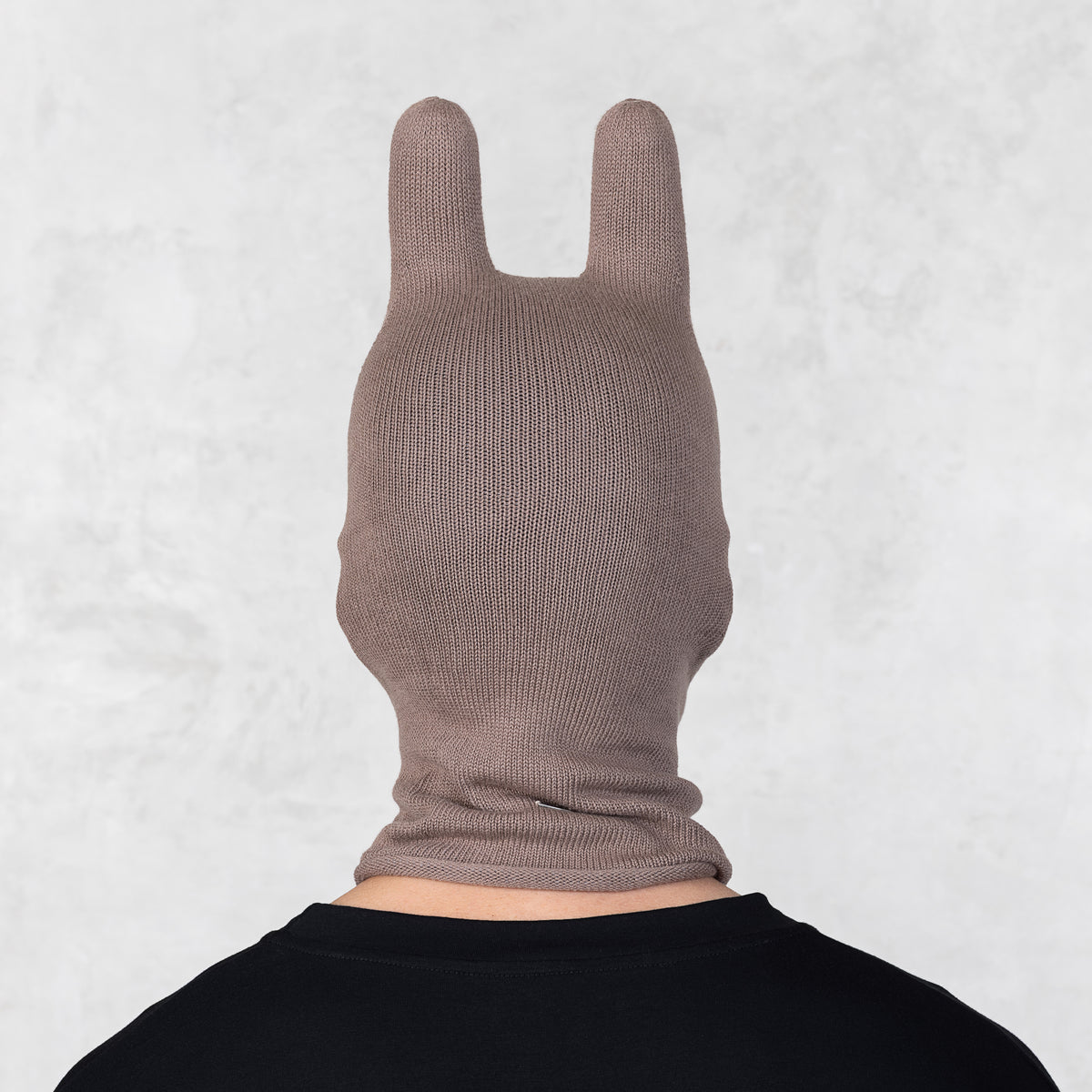 Person wearing a brown knit mask with ears on a light gray background