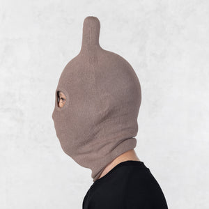 Person wearing a brown knitted balaclava with rounded ears on a light gray background