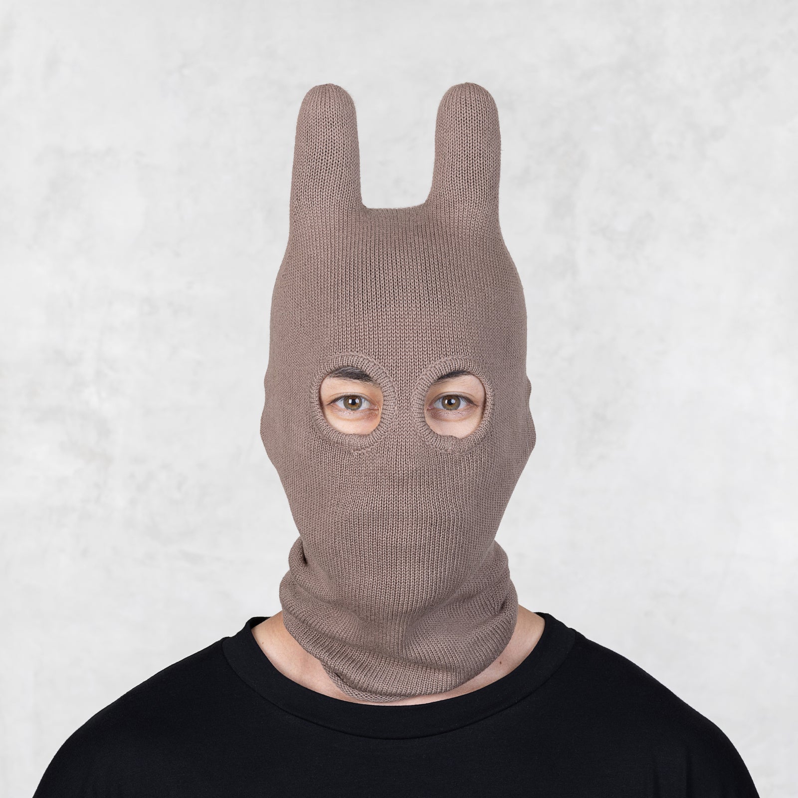 Person wearing a brown knit bunny mask against a light gray background