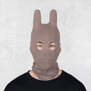 Person wearing a brown knit bunny mask against a light gray background